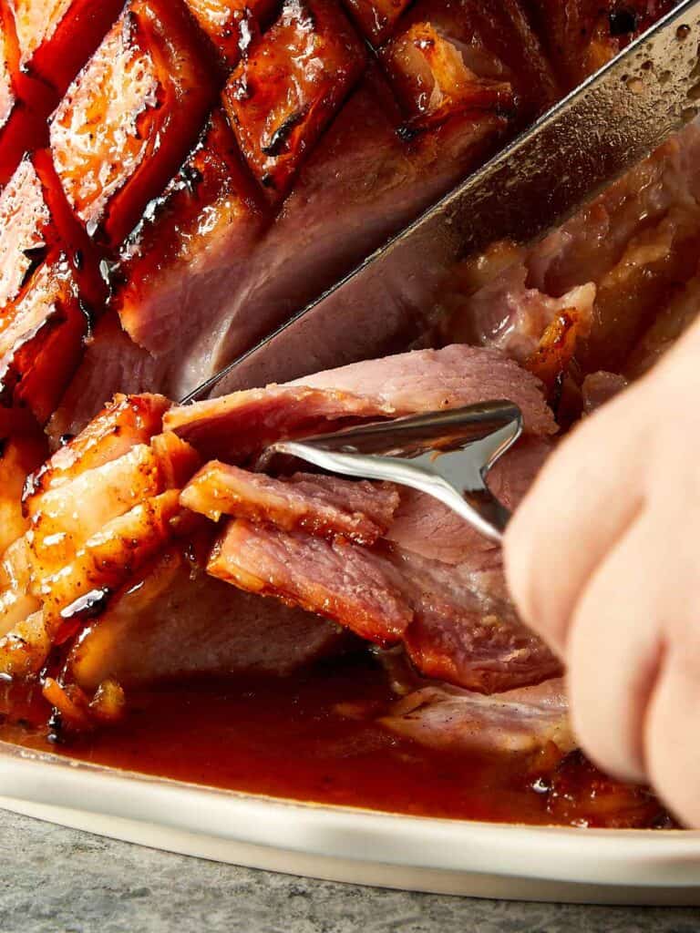 a side view of leg ham with a fork and a knife cutting the leg ham in slices - 17