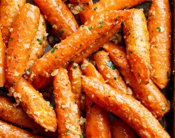 This close-up shot showcases a tantalizing dish of roasted carrots. Tightly packed together on a baking sheet, the carrots are a vibrant orange, glistening with a delicious glaze. A scattering of herbs, likely parsley, adds a touch of green and hints at a savory flavor profile. The edges of some carrots are slightly caramelized, promising a delightful sweetness and crunch.