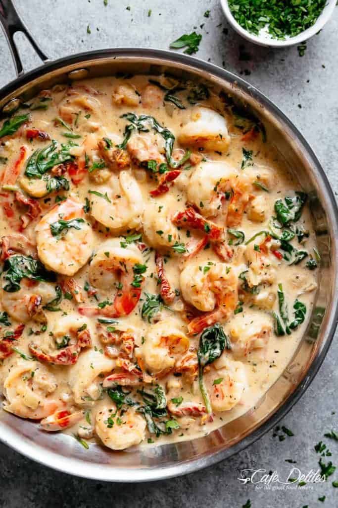 Creamy Garlic Butter Tuscan Shrimp coated in a light and creamy sauce filled with garlic, sun dried tomatoes and spinach! Packed with incredible flavours! | https://cafedelites.com