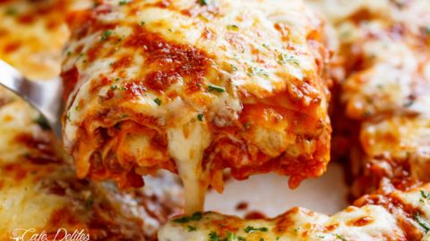 A beautiful close-up of a slice of lasagna being lifted by a spatula from the baking tray, showcasing layers of pasta, rich meat sauce, creamy cheese, and a golden, bubbly top.