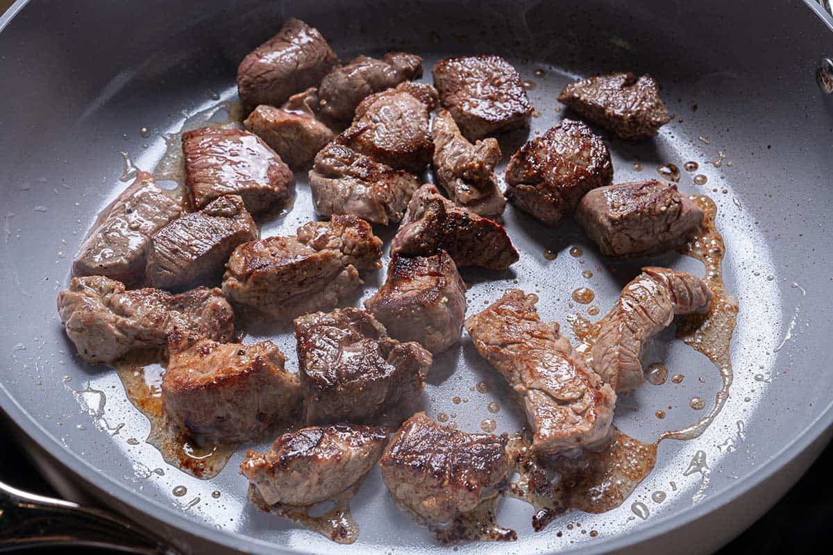 Steak Chunks being seared in a large pan over medium heat.