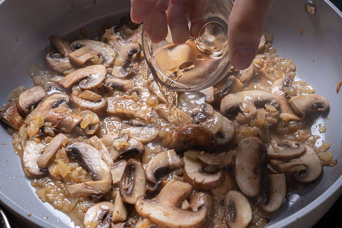 wine being added to the pan where vegetables are cooking.