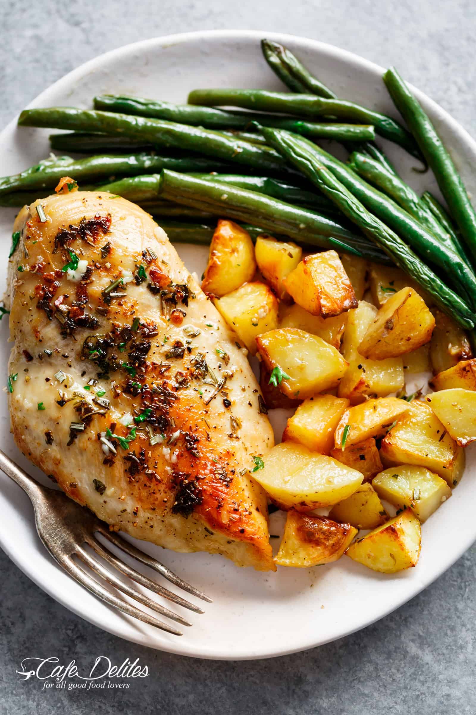 Green beans, crispy potatoes and a golden chicken breast on a plate with a fork ready to eat. 