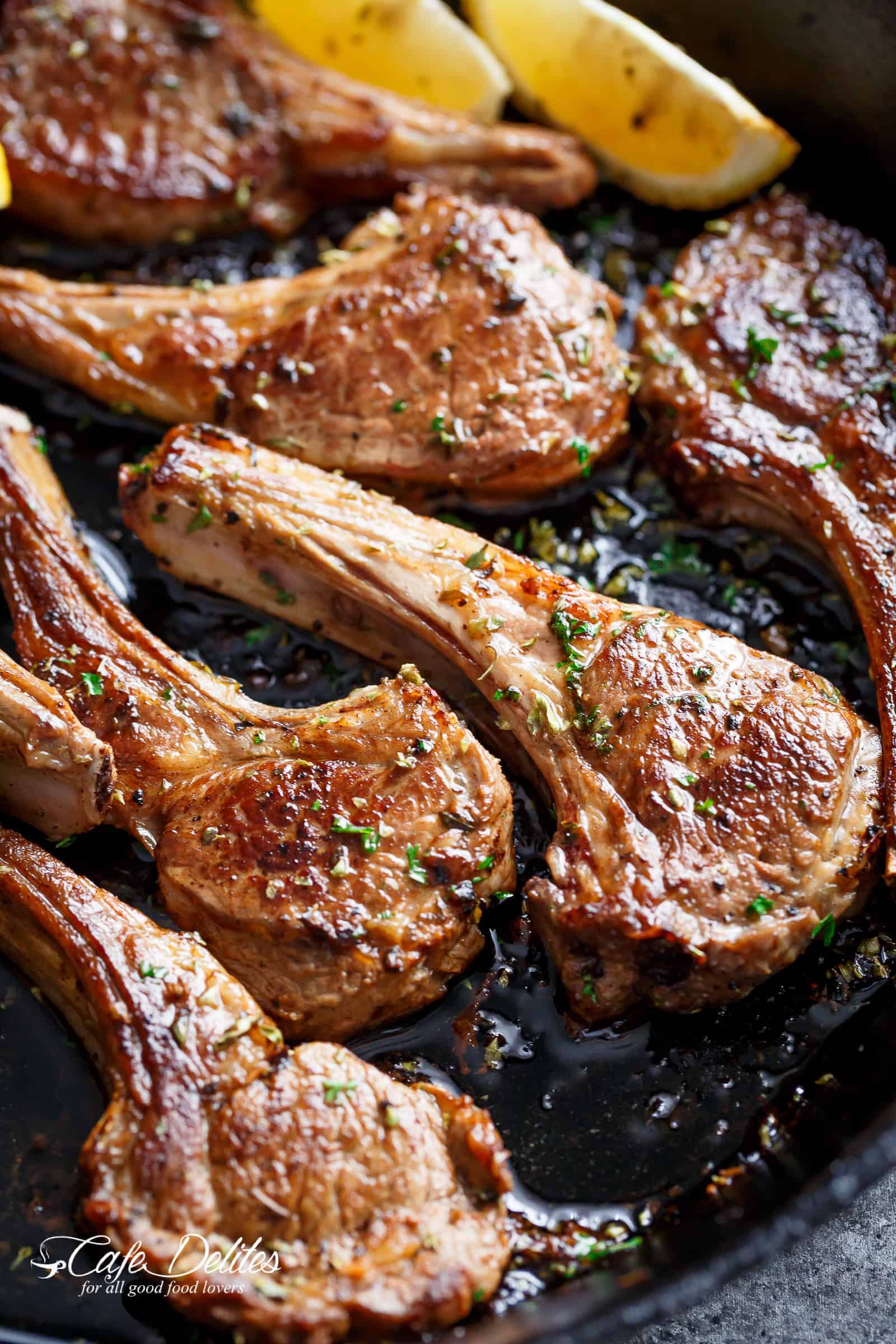 Several pieces of meat cooking in a skillet and seasoned with fresh herbs.