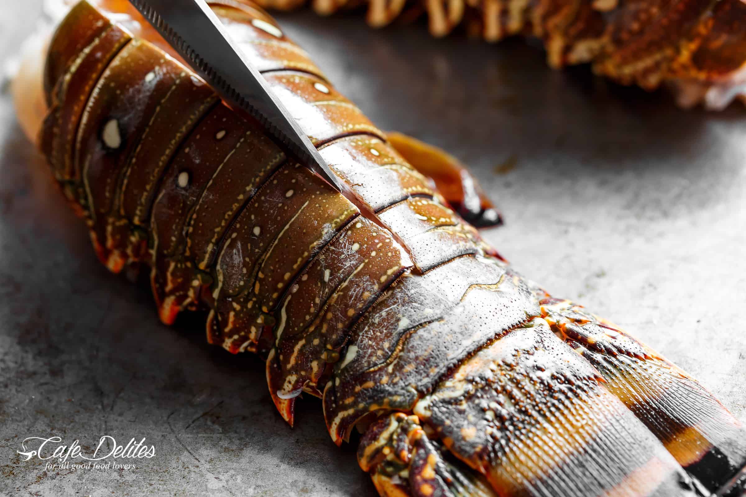 Close up on a knife cutting up a raw lobster tail.