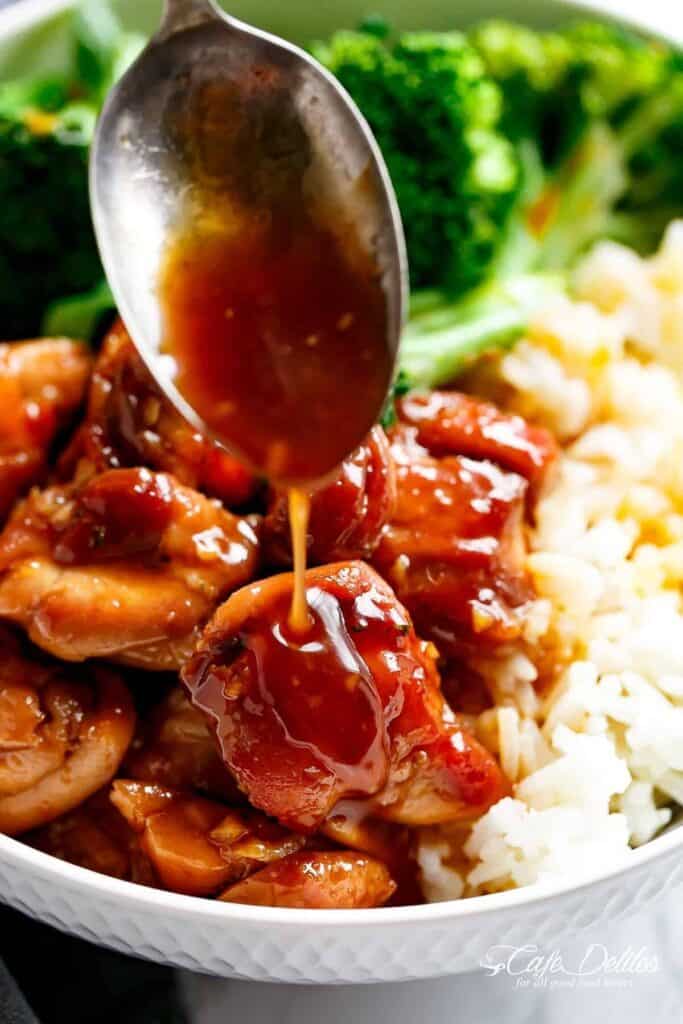 Close-up image of teriyaki chicken served in a white bowl, accompanied by teriyaki sauce, rice, and broccoli.