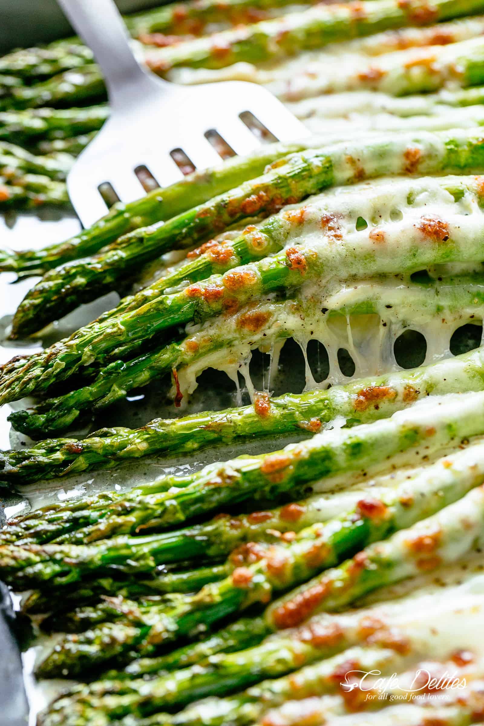 A silver spatula picks up a pile of five roasted asparagus spears topped with melted mozzarella cheese | cafedelites.com