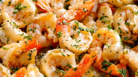 The shrimp are served in a pan, their pinkish-orange hues suggesting they are cooked to perfection. The shrimp are generously coated in a light sauce, which appears to be infused with herbs, as evidenced by the specks of green throughout the dish.