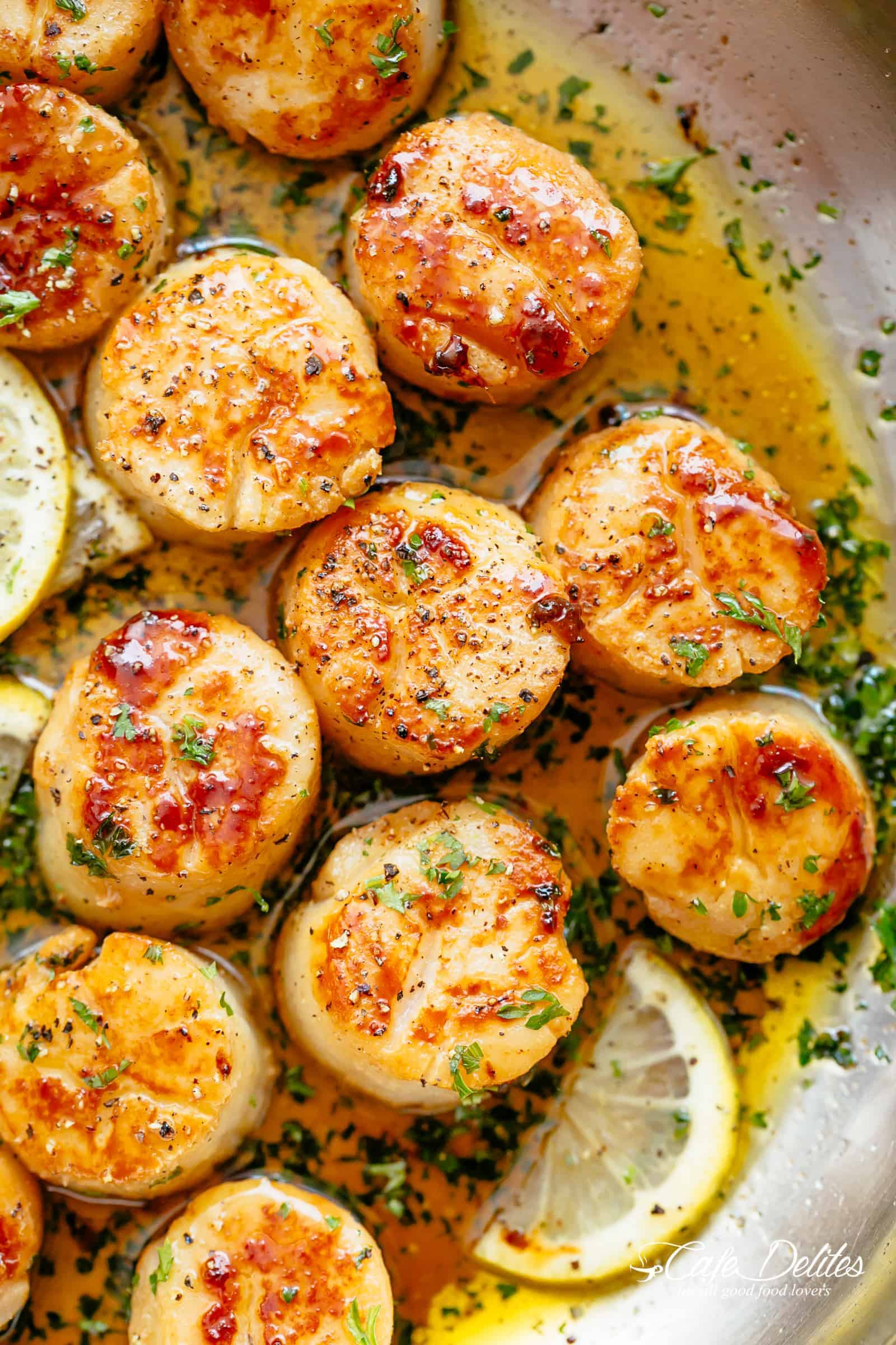 Close-up image of perfectly cooked scallops garnished with freshly cut parsley.