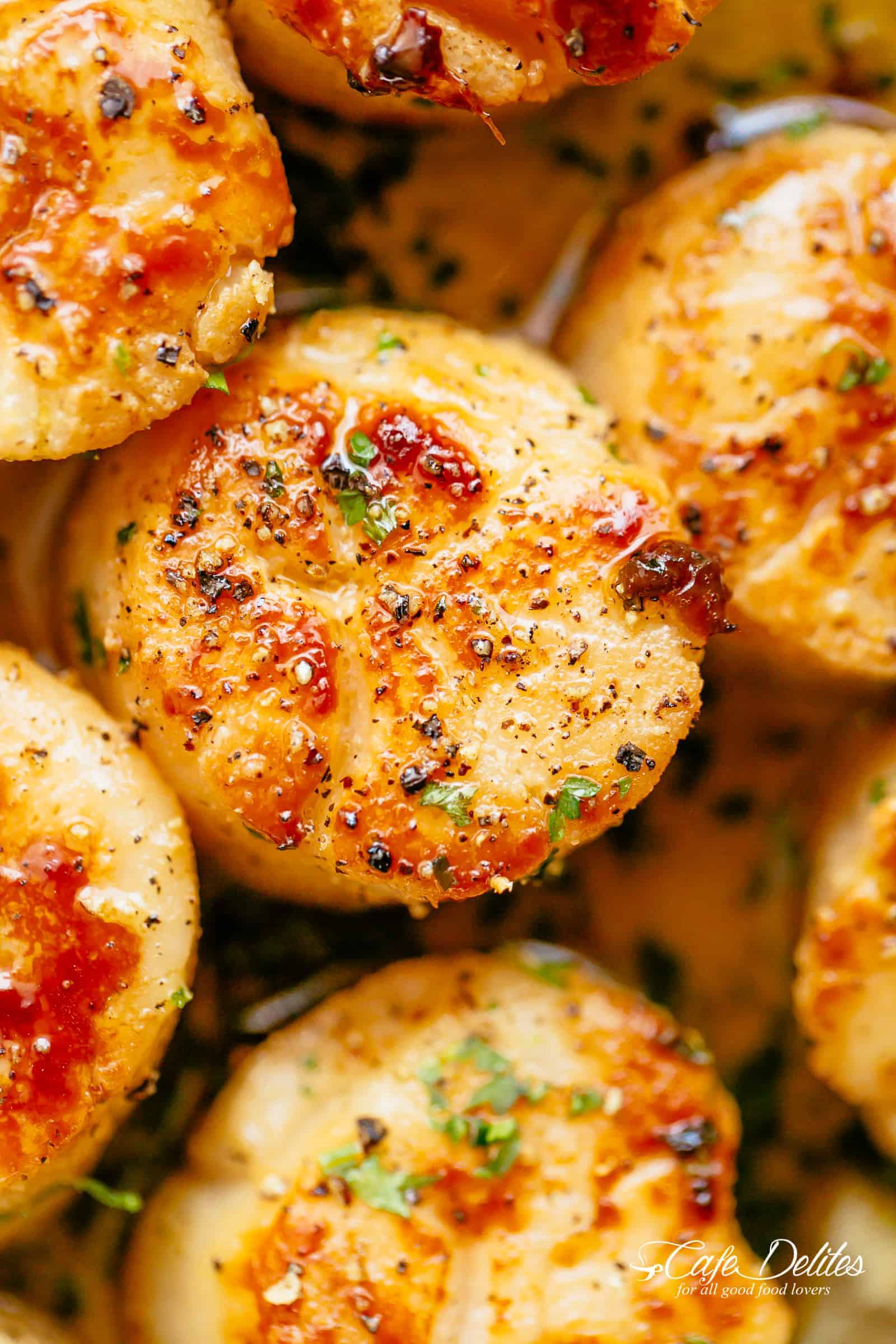 Close up of crispy scallop covered in course salt, pepper and finely chopped green herbs. 