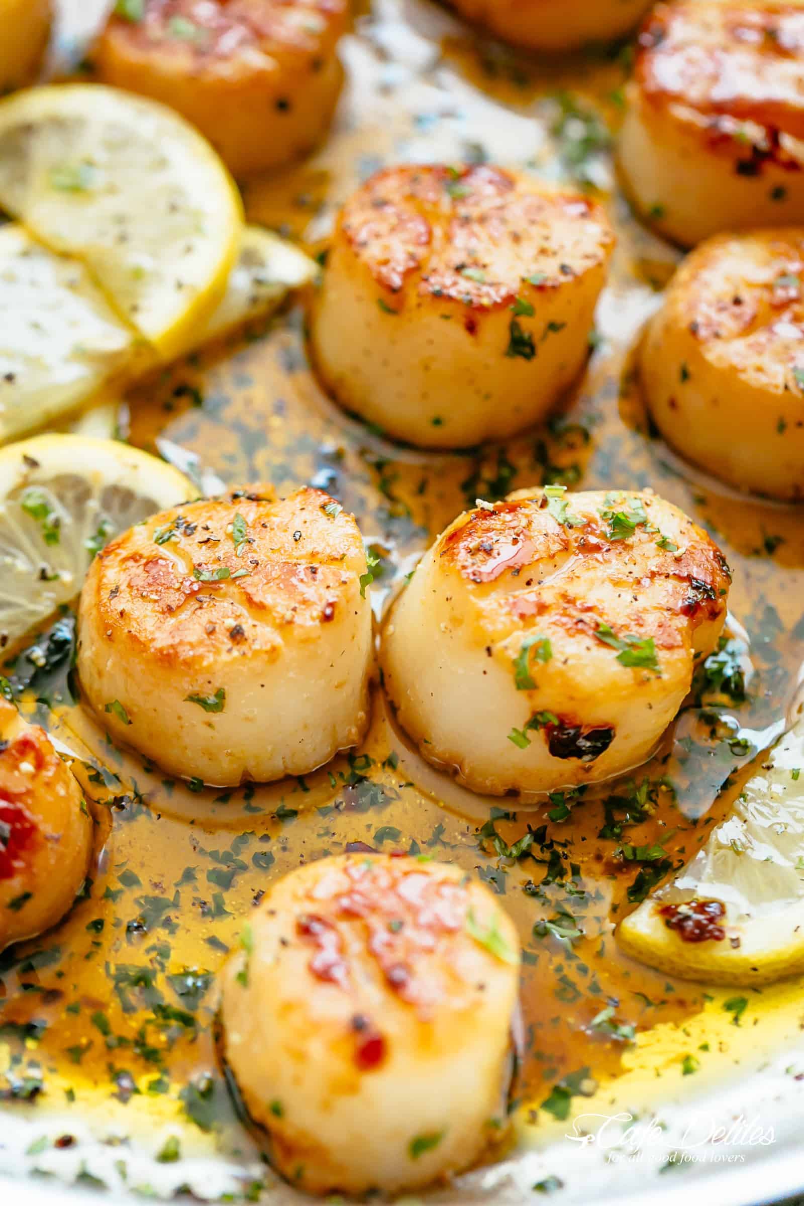 Close up of lemon garlic butter scallops resting in melted garlic butter sauce, surround by thin lemon wedges. 