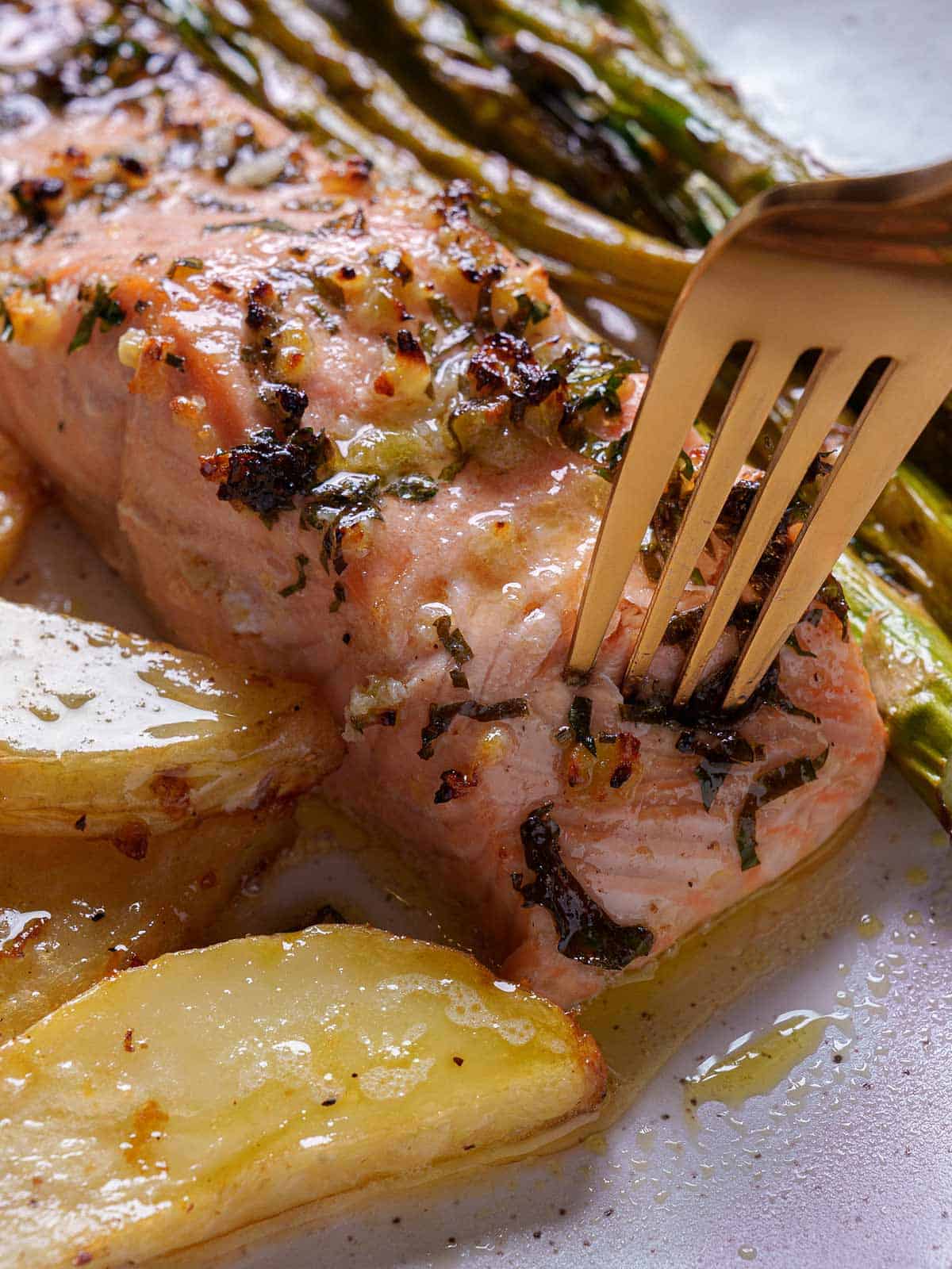 Close-up of a perfectly cooked salmon fillet, gently pulled apart by a golden fork, revealing its flaky and tender texture.