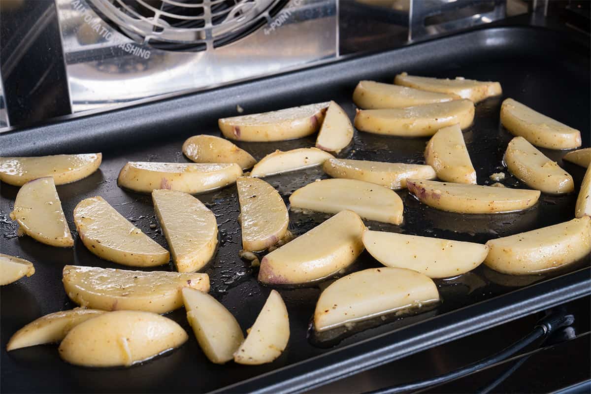 Image of potatoes being tossed in the oven, arranged on a large rimmed baking sheet for roasting