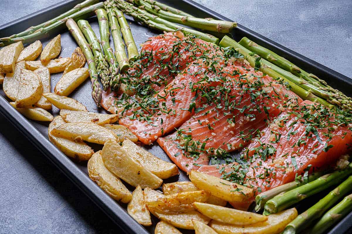 Image of potatoes, asparagus, and salmon being arranged on a baking sheet before being placed into the oven.