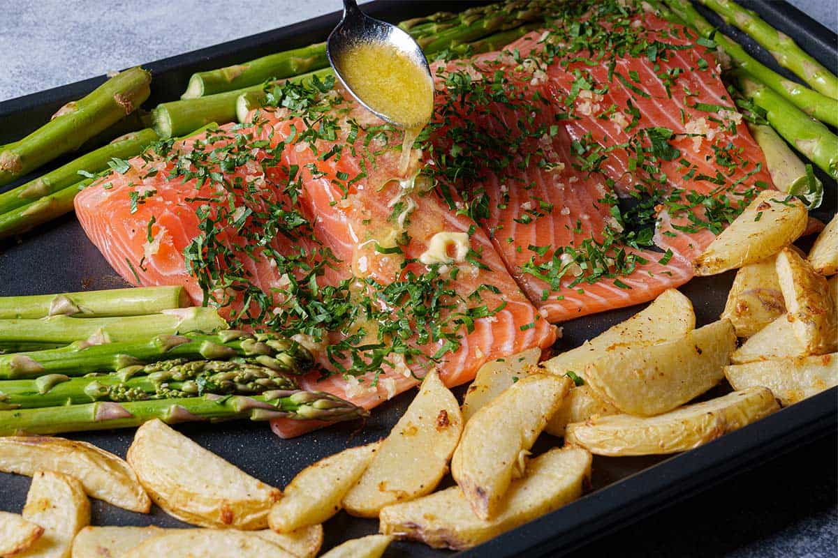 Image of lemon juice and melted butter being poured over the salmon on a baking sheet.