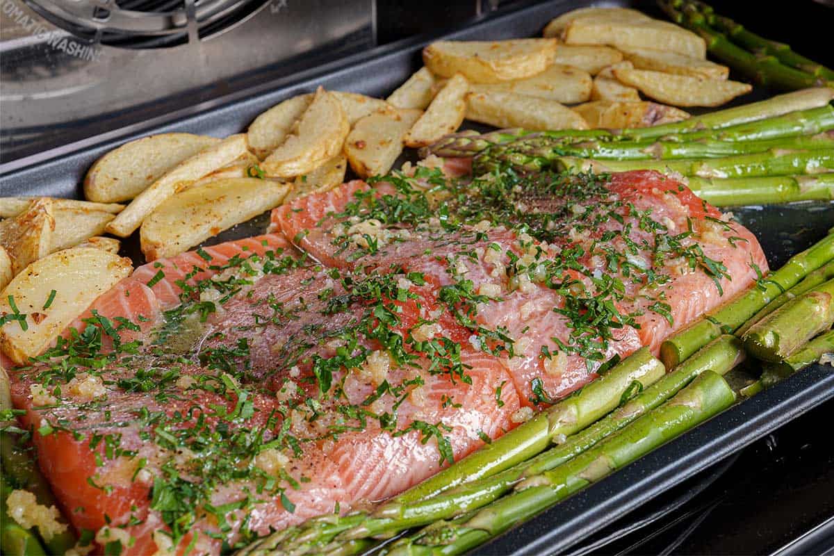 Salmon, potatoes, and asparagus being cooked in the oven until fully cooked through.