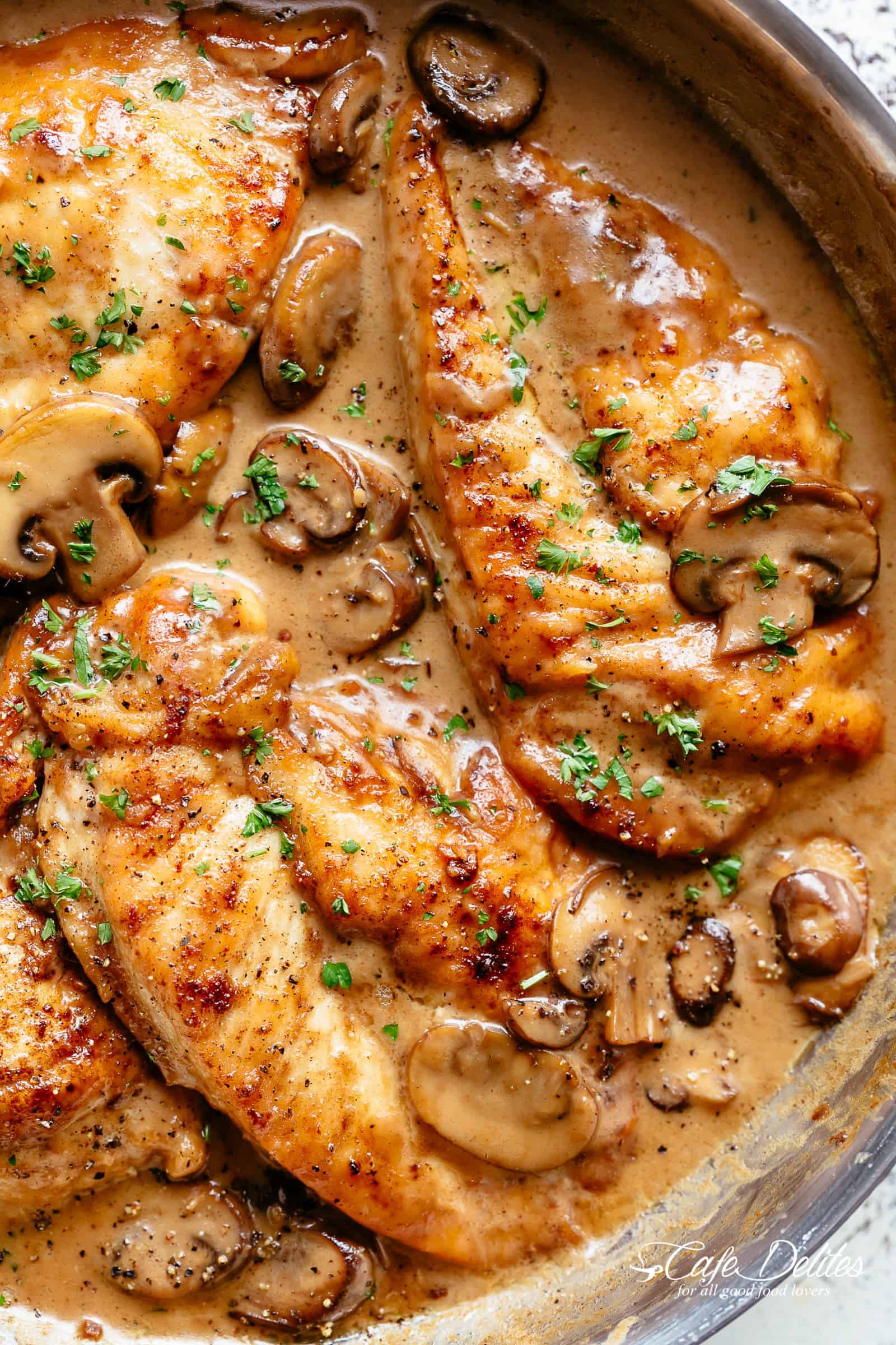 Close up of chicken breasts in a pot submerged in Marsala sauce with fresh herbs sprinkled on top. 