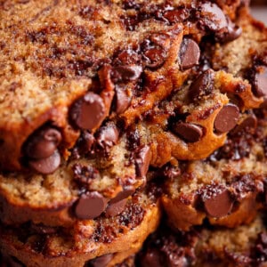 freshly baked banana bread has a golden brown crust and the inside is a pale yellow color. The bread is studded with chocolate chips that have melted slightly, creating a gooey texture within the slices. The camera is zoomed into a stack of these slices, emphasizing the moist texture and abundance of chocolate chips within each piece.