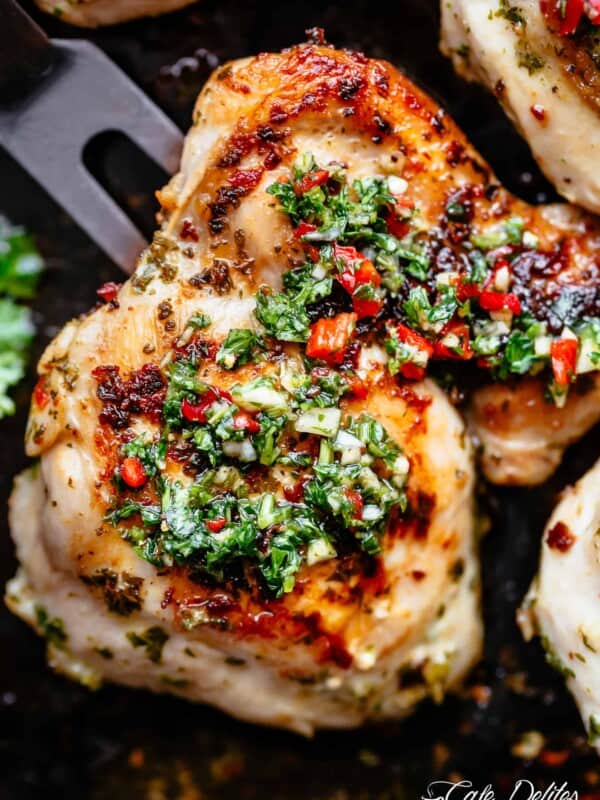 Golden roasted chicken on a black pan with Chimichurri on top.