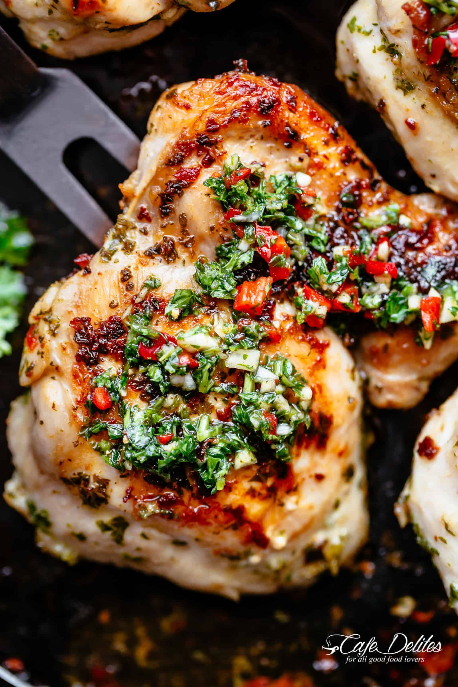 Golden roasted chicken on a black pan with Chimichurri on top.