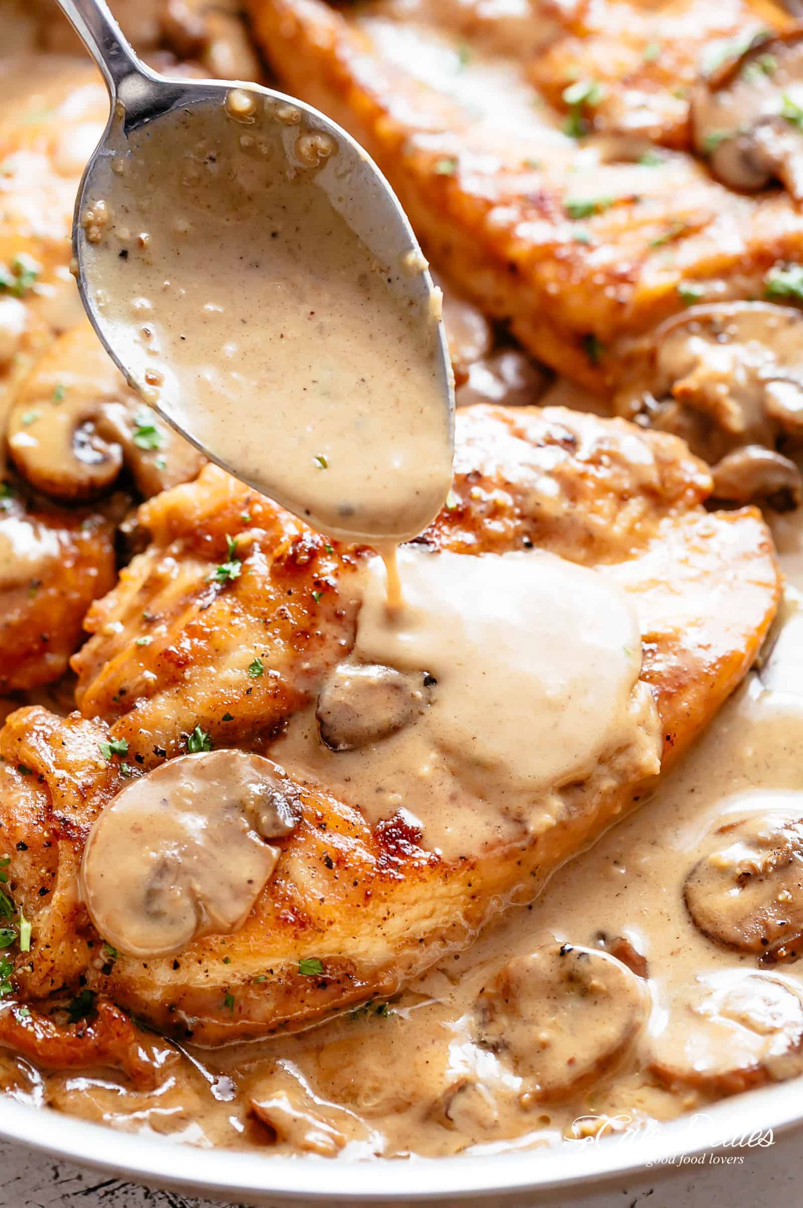 A spoon pouring creamy Marsala sauce over chicken breasts and mushrooms. 