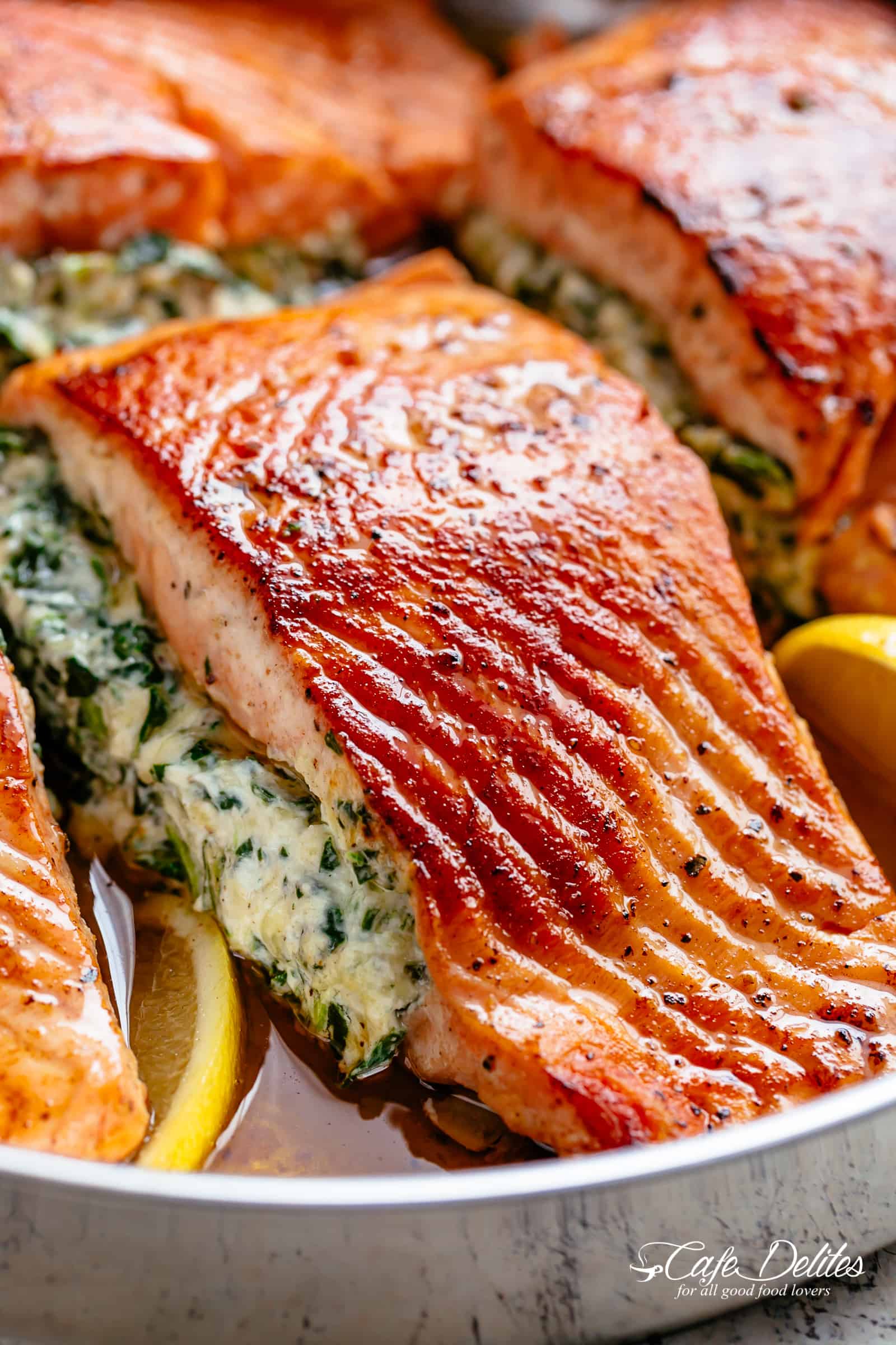 A close up image of a fillet of creamed spinach stuffed salmon in a silver pan with lemon slices | cafedelites.com