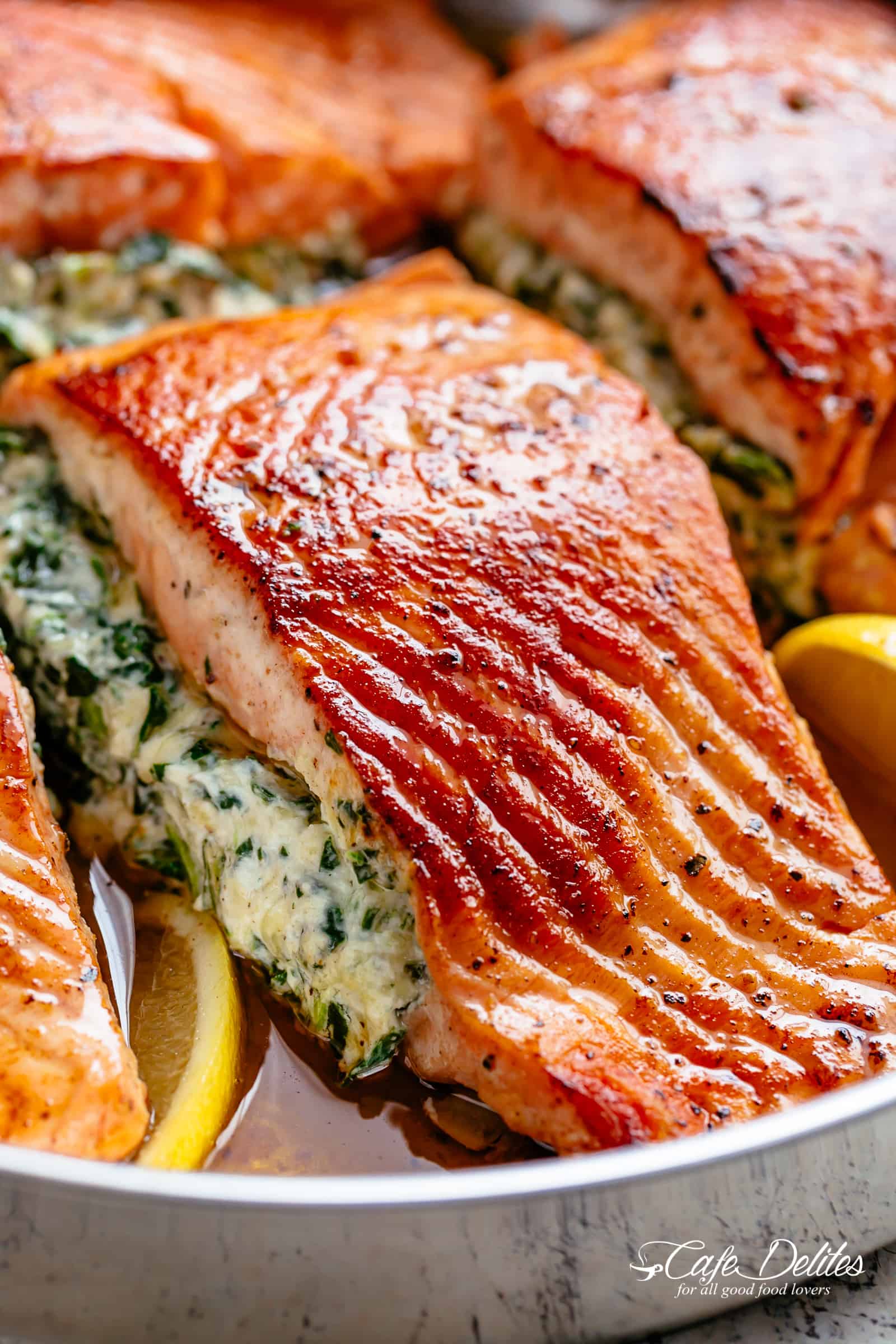 A close up image of a fillet of creamed spinach stuffed salmon in a silver pan with lemon slices 