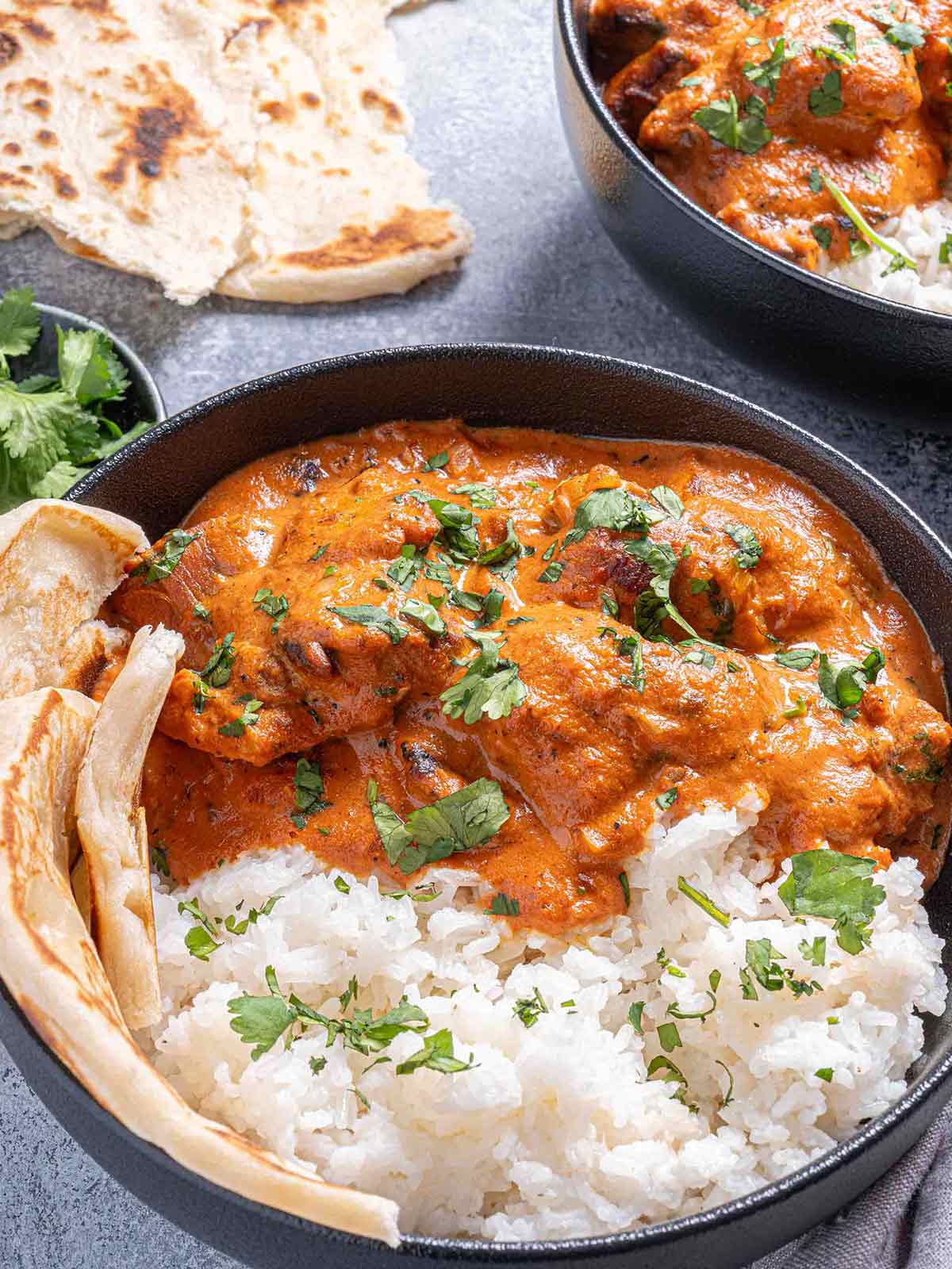 chicken tikka masala in a bowl garnished with fresh parsley, served beside rice with naan 