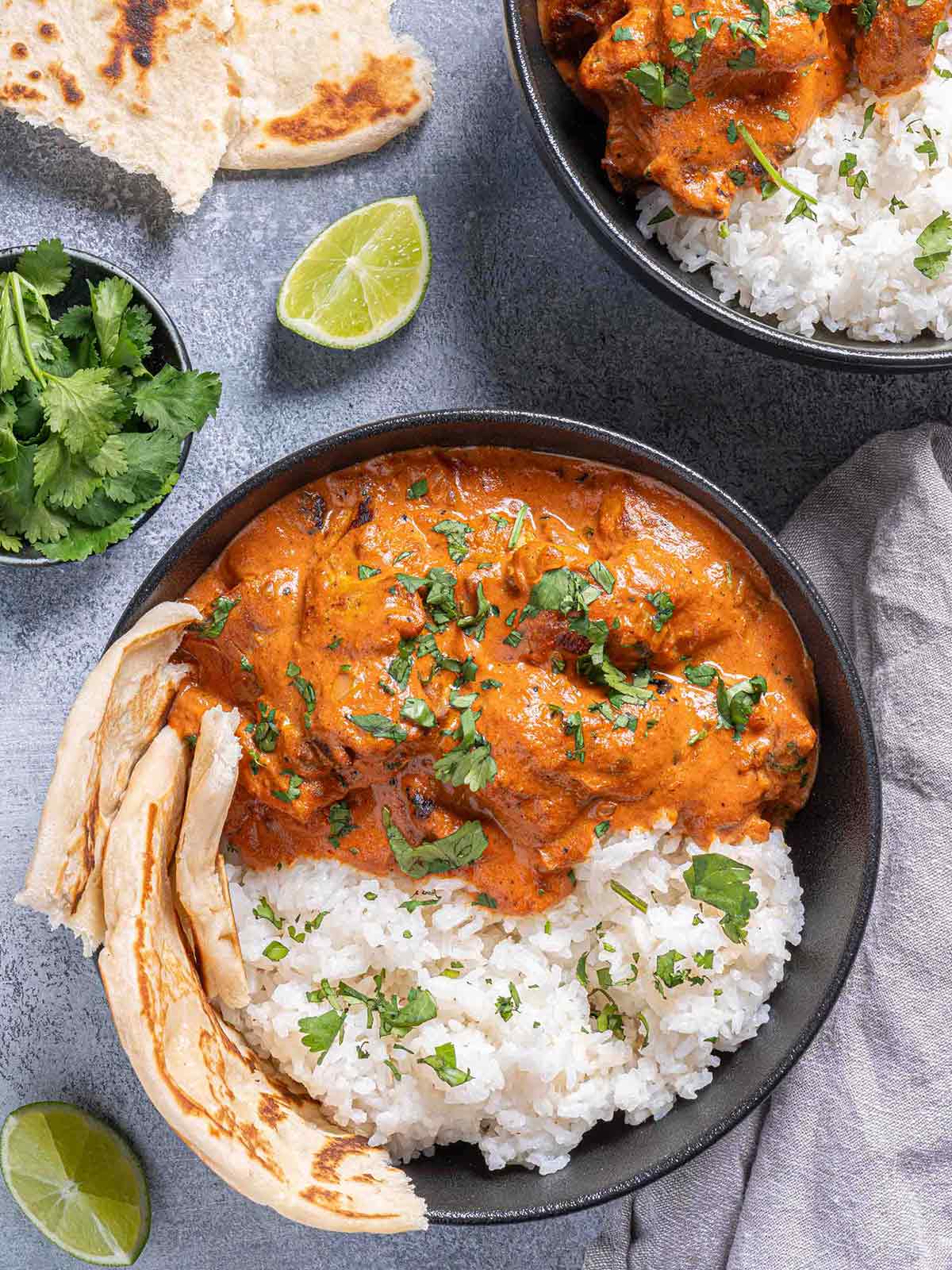 chicken tikka masala in a bowl garnished with fresh parsley, served beside rice with naan 