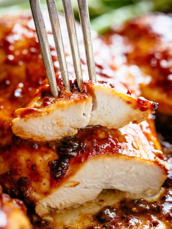 a side view of chicken breast cut in two and stacked one top of another with a fork piercing the top slice covered in a honey mustard glaze