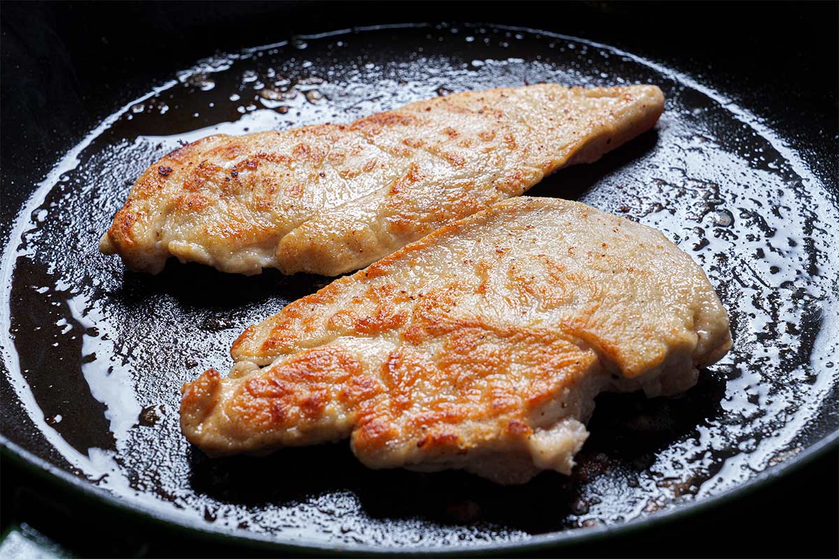 Image of chicken breasts being pan-fried in oil and butter.