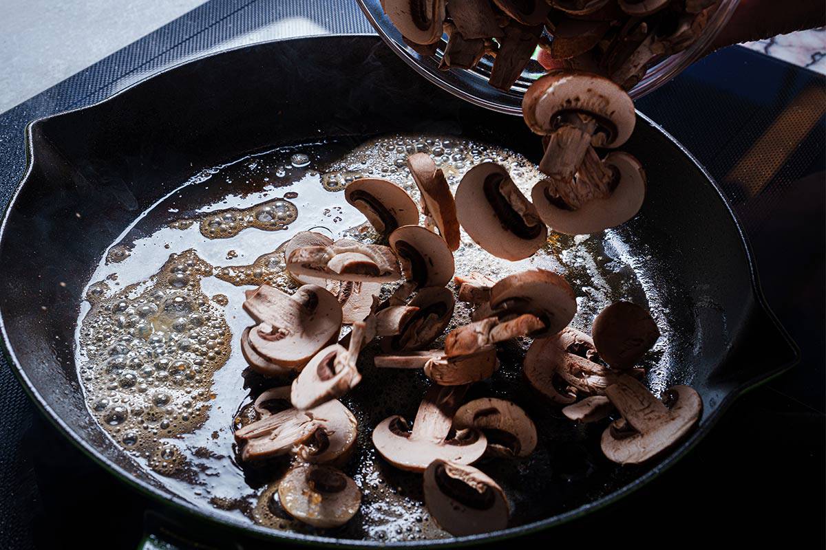 An image of mushrooms being added to the same pan with the remaining grease from the chicken.