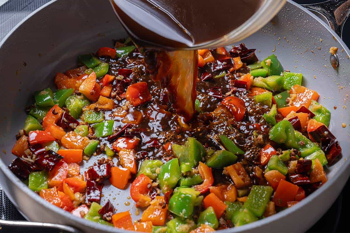 garlic, ginger, chili diced peppers (capsicums) and Sichuan peppercorns with a sauce mixture being poured into the wok