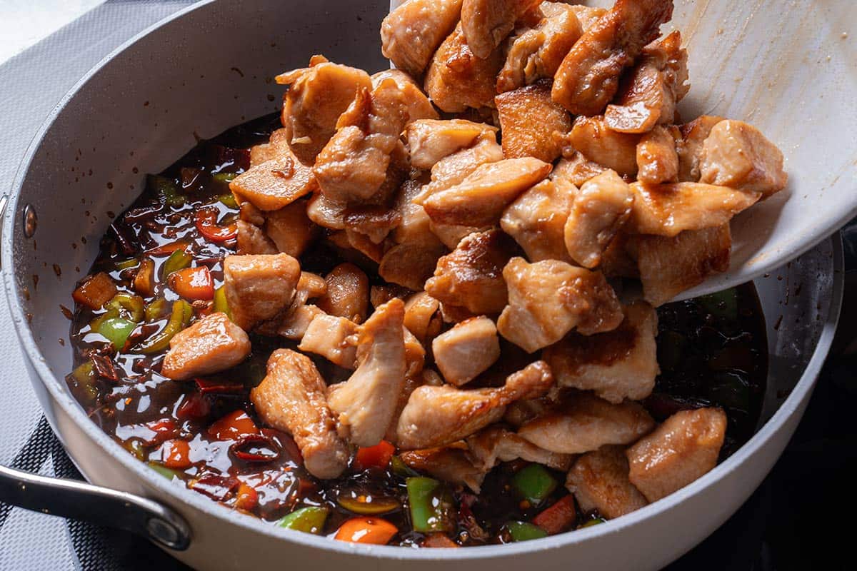 garlic, ginger, chili diced peppers (capsicums) and Sichuan peppercorns and sauce mixture with cooked chicken being poured in