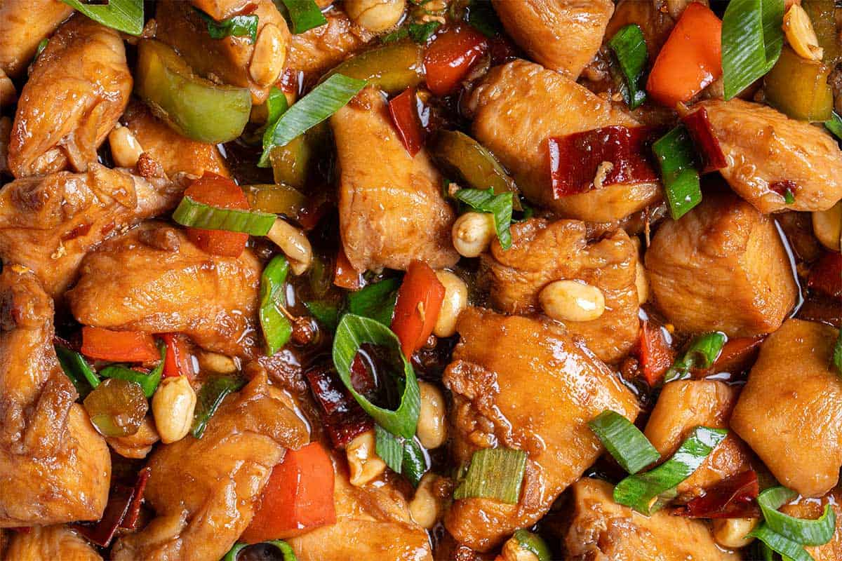 Close up image of Kung Pao Chicken in a sticky Kung Pao sauce with green and red chopped vegetables picked in with chicken pieces. 