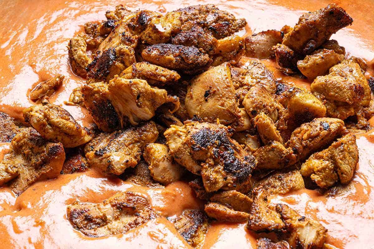 creamy tikka masala sauce with seared chicken being poured in