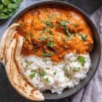 chicken tikka masala in a bowl garnished with fresh parsley, served beside rice