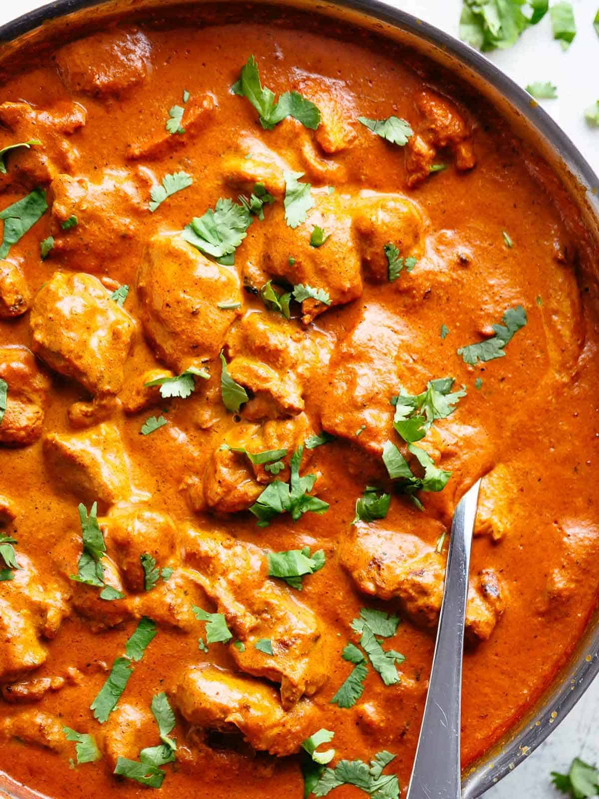 chicken tikka masala in a bowl garnished with fresh parsley, served beside rice with naan