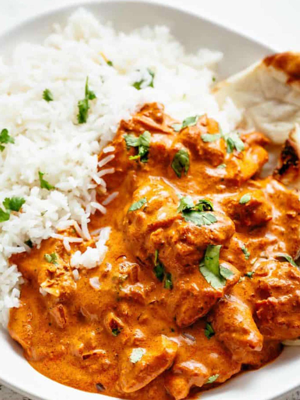 chicken tikka masala in a bowl garnished with fresh parsley, served beside rice