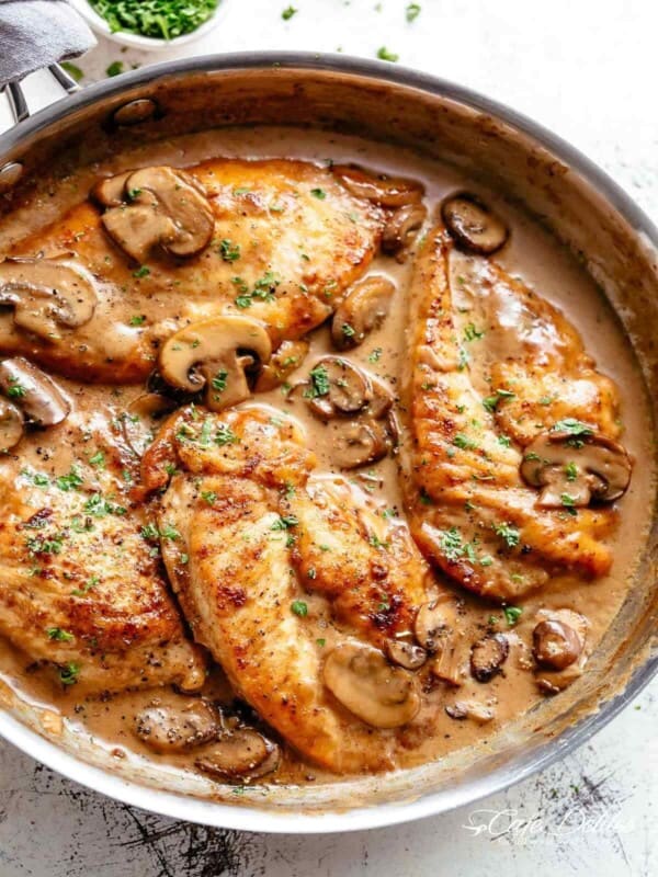 Chicken breasts in a creamy, brown marsala sauce with mushrooms and fresh herbs in a pan.