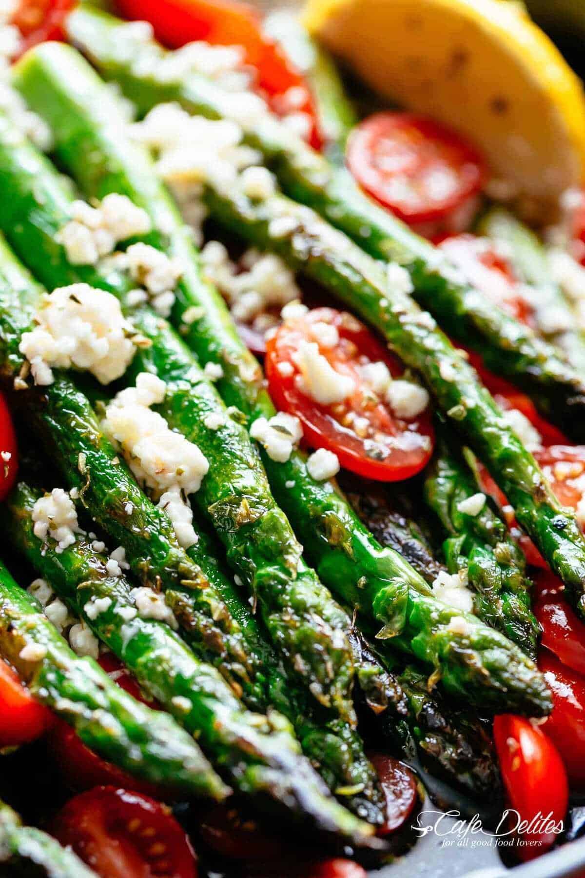 close up image of light browned, crunchy asparagi topped with feta cheese and tomatoes.