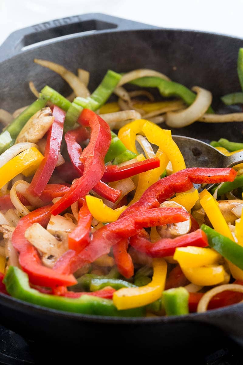 Yellow, green, and red bell peppers cooking in a skillet