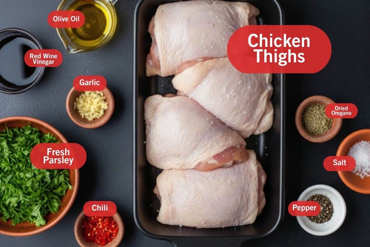 flat lay photo of ingredient shot of chicken thighs, dried oregano, salt, pepper, chili, fresh parsley, garlic, red wine vinegar, olive oil