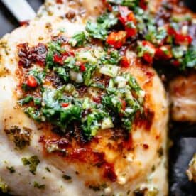 Golden roasted chicken on a black pan with Chimichurri on top.