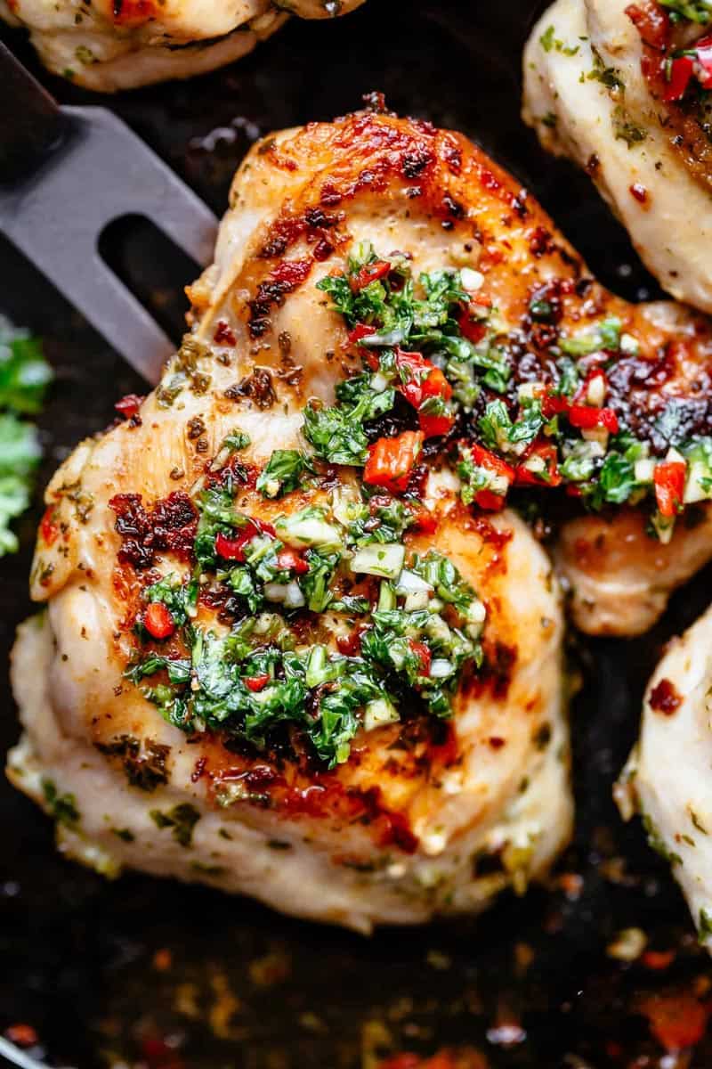 Golden roasted chicken on a black pan with Chimichurri on top.