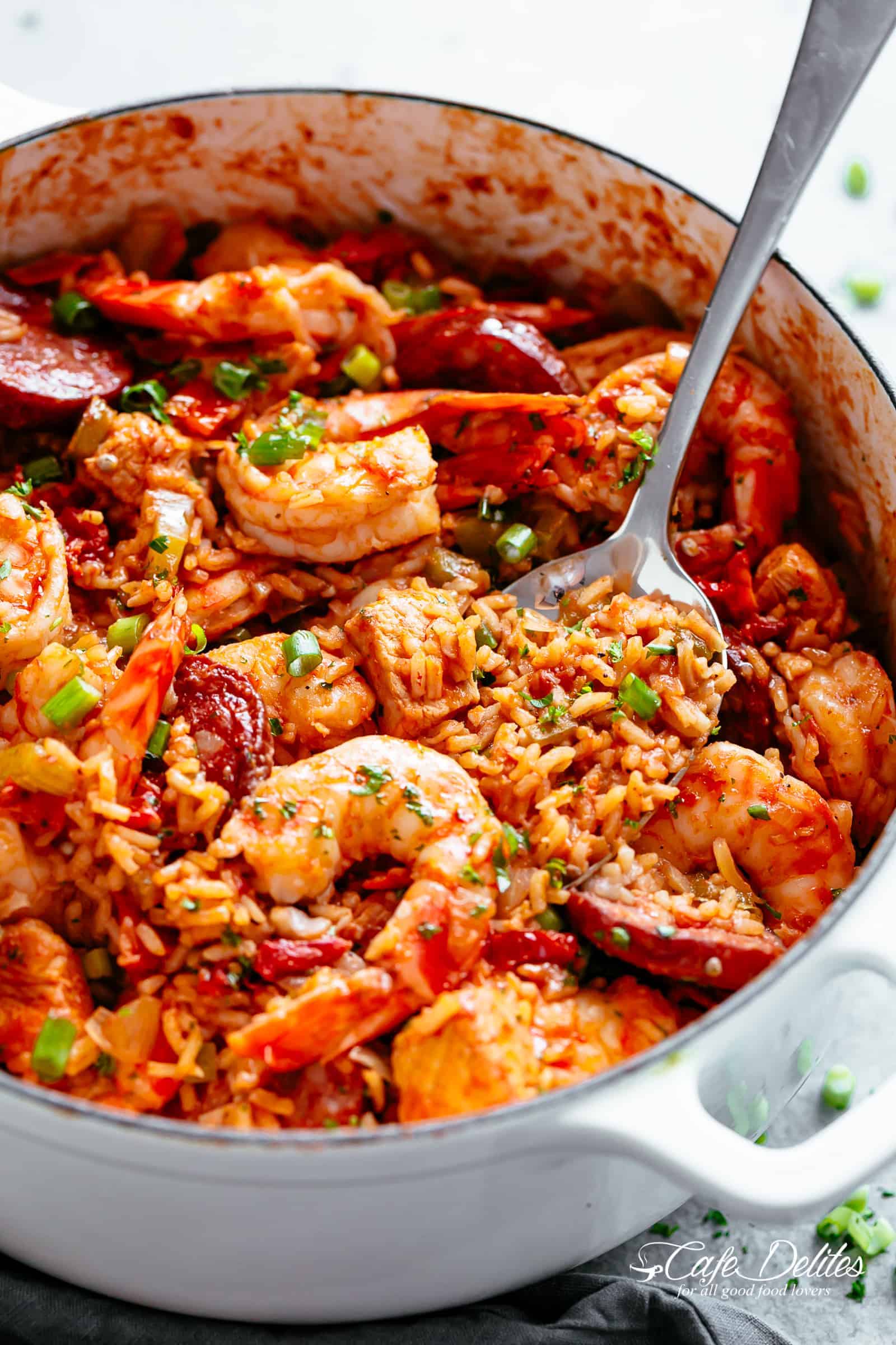 Spoonful of red rice resting in dutch oven pot full of jambalaya. 