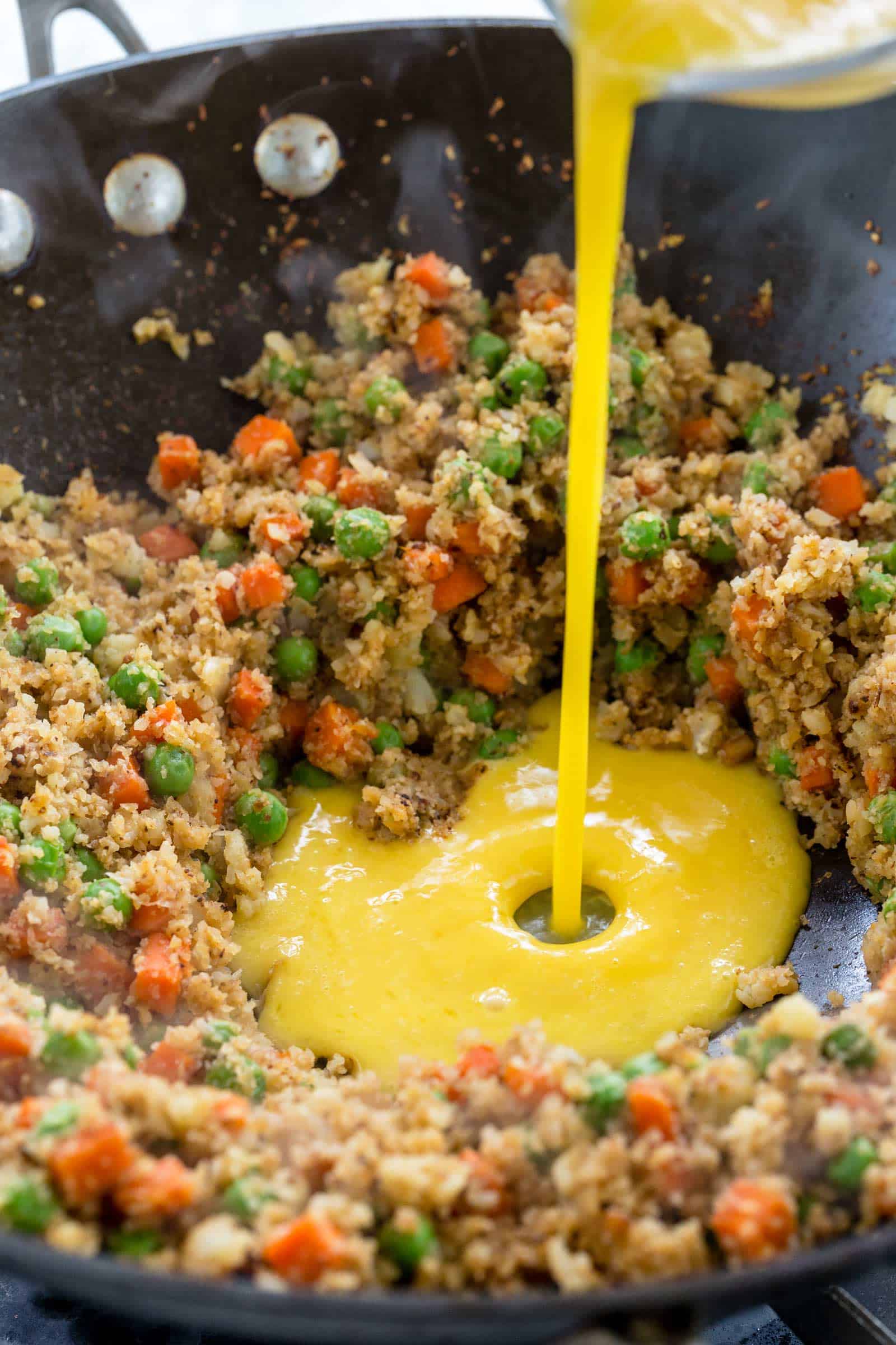 pouring egg mixture into a wok with cauliflower rice