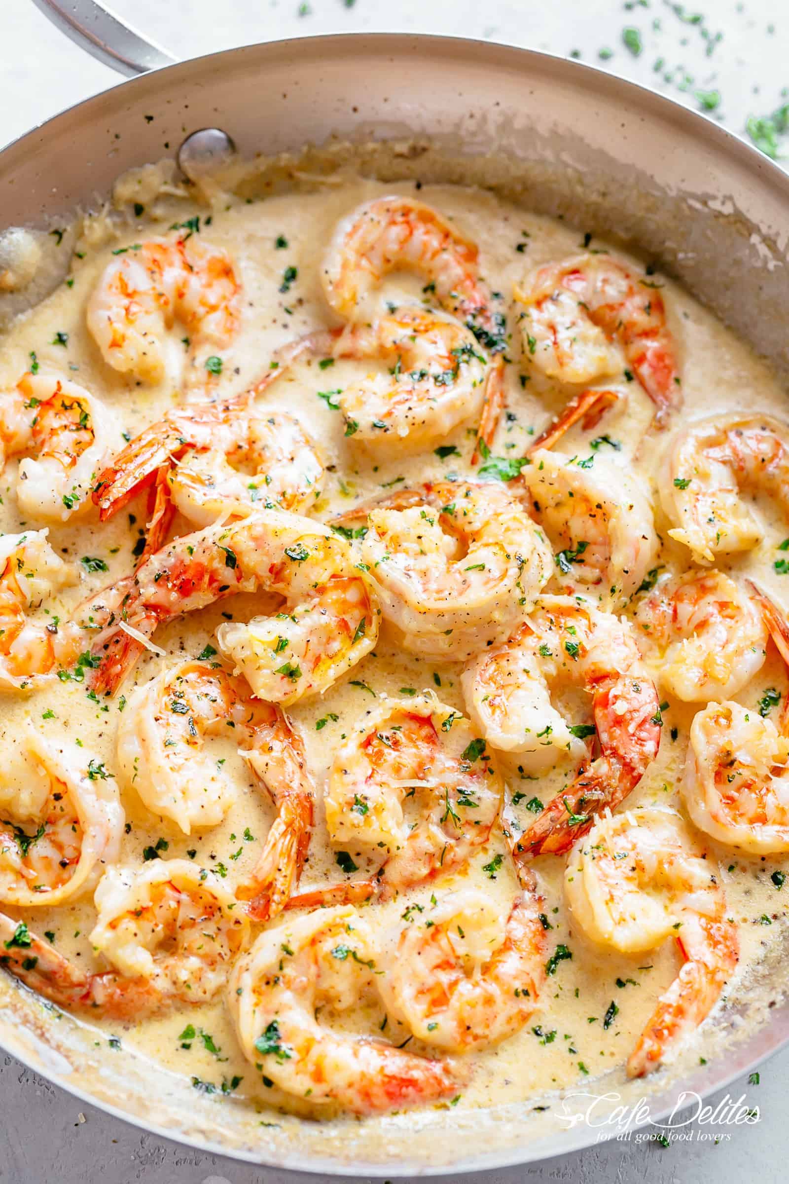 Creamy Garlic Shrimp in a silver frying pan garnished with fresh chopped parsley on a light grey background. A deliciously easy Shrimp Recipe coated in a rustic and buttery sauce ready in less than 10 minutes, people will think there is a hidden chef in your kitchen! Transform ingredients you most likely already have in your refrigerator into an incredible dinner! | cafedelites.com