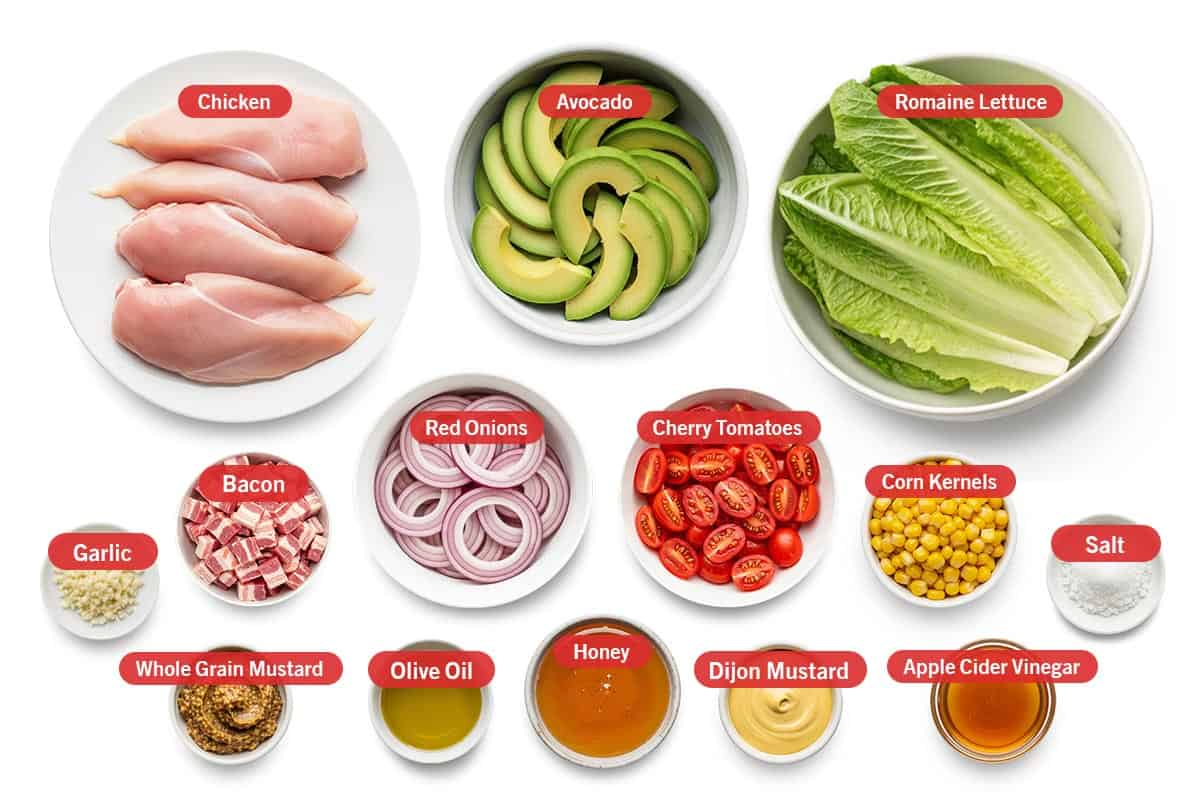 Top shot of ingredients: Chicken, avocado, Romaine lettuce, garlic, bacon, red onion, cherry tomatoes, corn kernels, salt, whole grain mustard, olive oil, honey, Dijon mustard, and apple cider vinegar