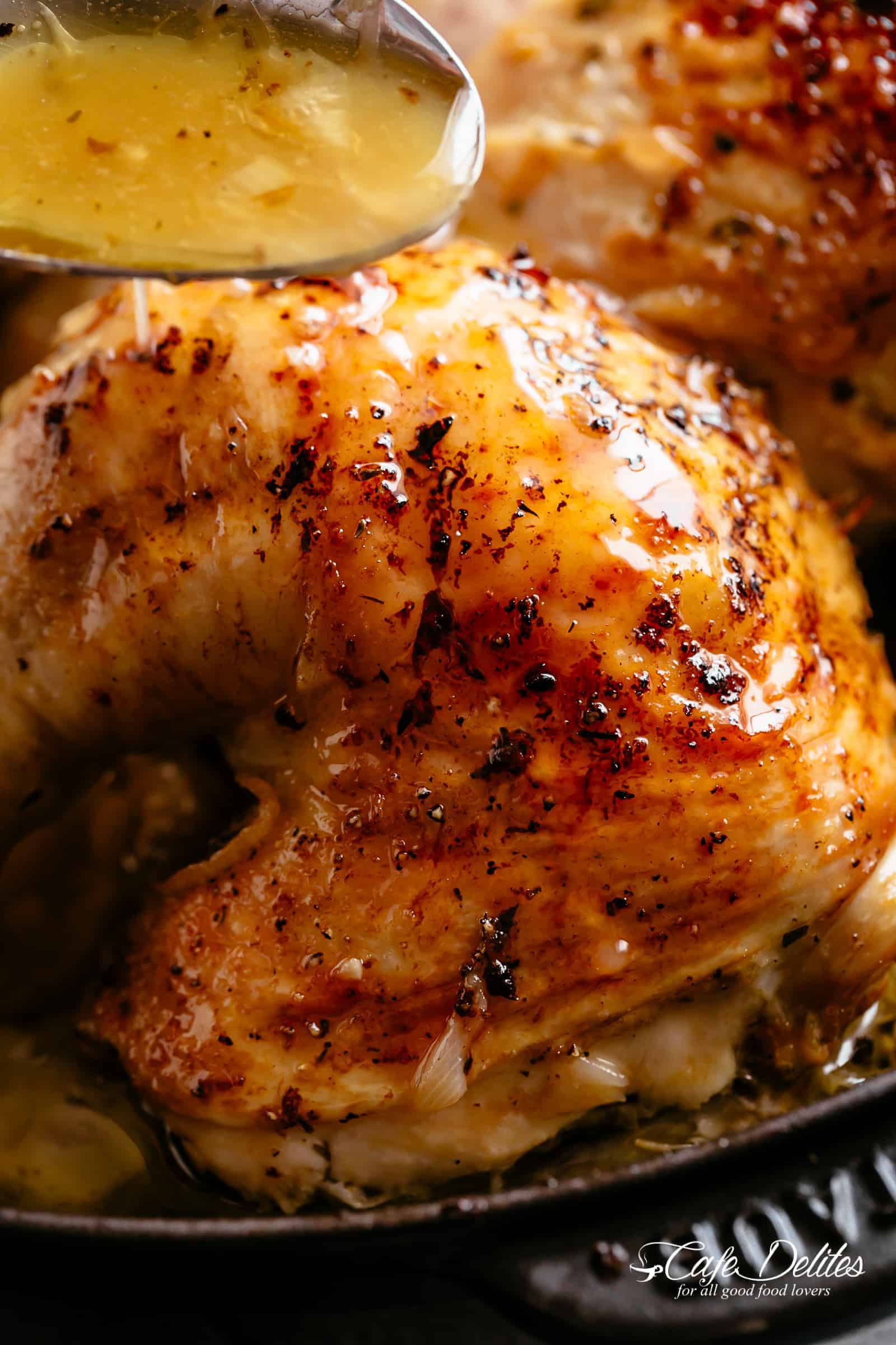 Pan juices being poured with a tablespoon onto a crispy leg. 